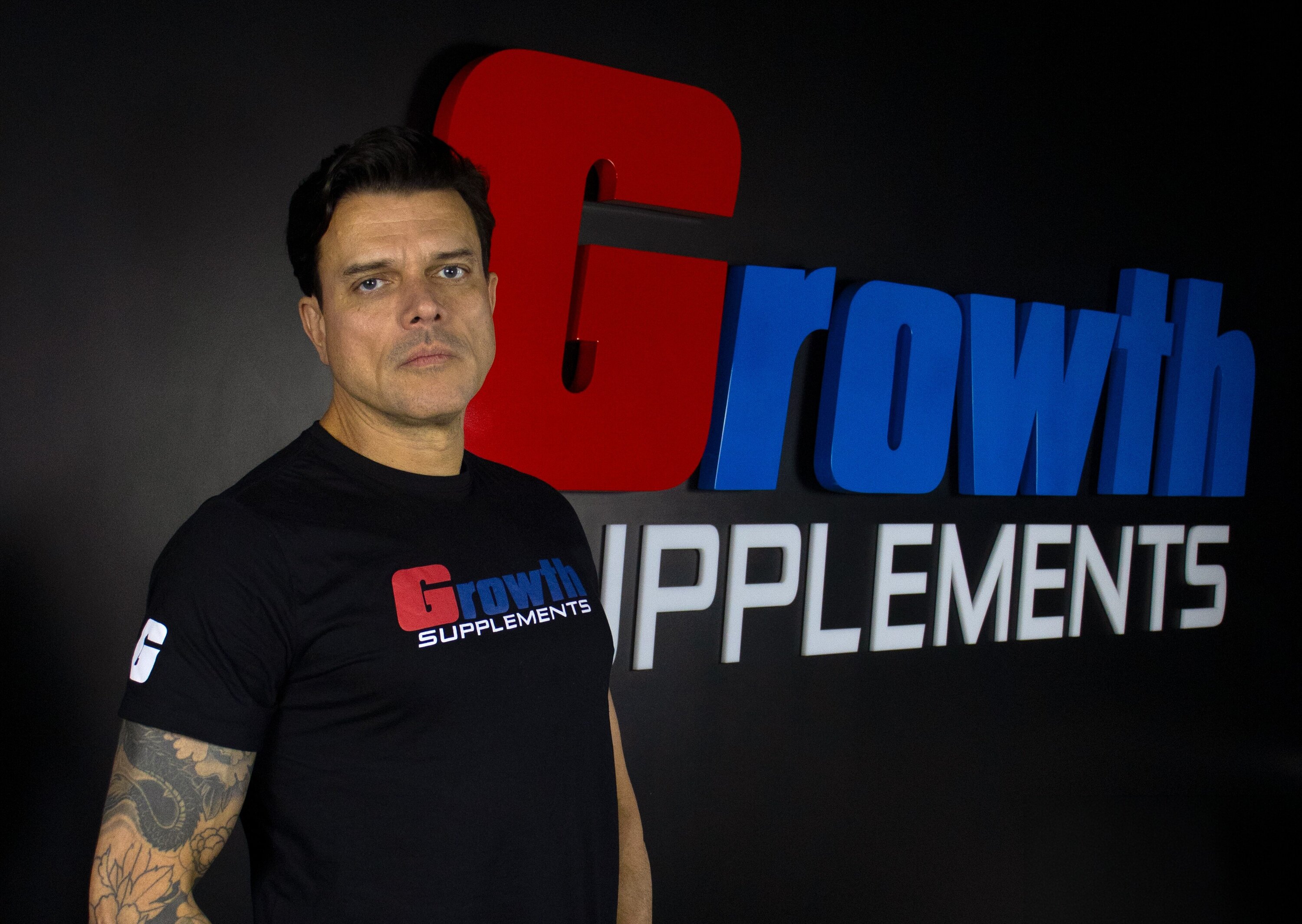 Ricardo Felix, gerente nacional de varejo da Growth Supplements, ao lado de placa com nome da marca